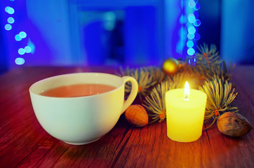 Cup of hot tea on a wooden table with candle, nut and pine trees on a winter evening