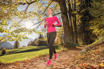 Young, sexy woman runs through a colorful autumn forest in the mountains - she is doing her running workout outdoor at a beautiful sundown and a amazing landscape