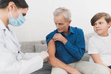Fototapeta premium A nurse makes an insulin shot of an old man. A nurse is sitting in a mask and gloves on the couch.