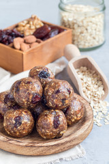 Obraz na płótnie Canvas Healthy energy balls with cranberries, nuts, dates and rolled oats on wooden plate, vertical