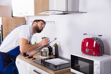 Technician Writing On Clipboard In Front Of Kitchen Extractor