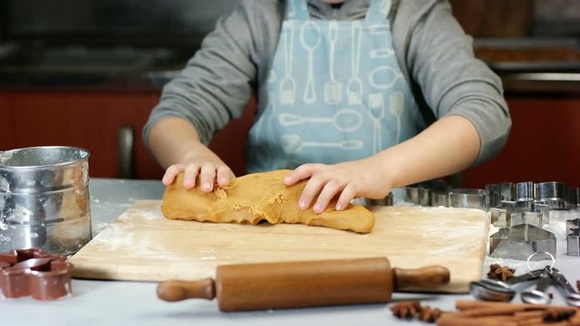 Five years old boy kneads the dough for christmas gingerbread cookies. Metal cutters, flour and rolling pen on a wooden table