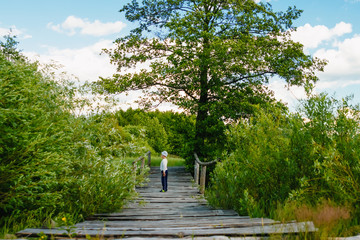Baby boy stands on a wooden bridge over a river and blue sky