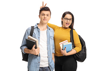 Female teen student pranking a male teen student with bunny ears