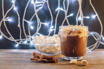 Hot chocolate, cinnamon sticks and marshmallow on the background of burning garlands, Christmas decorations, close up
