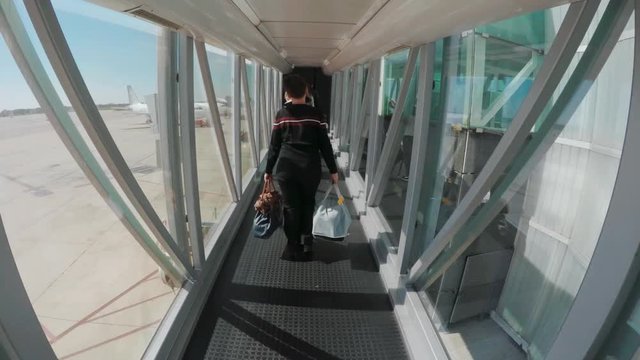 Woman walking in flight connections with baggage in hands. Airpport hub or tunnel to airplane, back view.