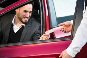 Valet Giving Receipt To Businessperson Sitting Inside Car