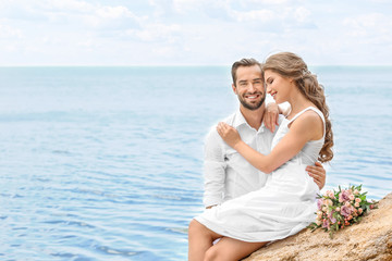 Happy newlywed couple sitting on rocky beach