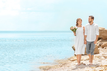 Happy newlywed couple walking on rocky beach