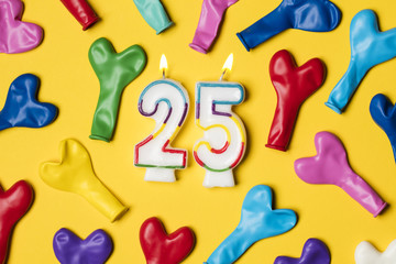 Number 25 candle with party balloons on a bright yellow background