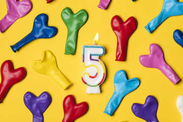 Number 5 candle with party balloons on a bright yellow background