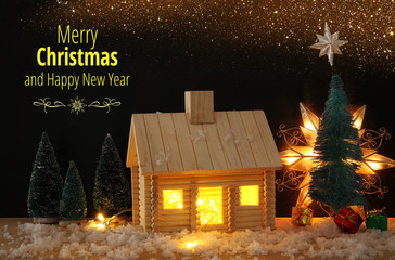 Image of christmas tree and wooden house with light through the window, over snowy table.