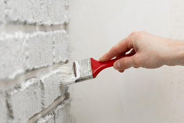 Male's hand painted with brush white brick wall.