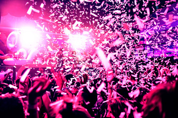 Confetti fired in the air during a in a disco. Hundreds of hands to the sky. Purple, magenta an pink tone/background with hard contrast