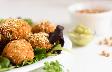 Falafels, spicy chickpea balls with parsley, cumin and semin seeds, put on a plate with salad and cherry tomatoes. One chickpea ball is broken open. Falafel are served with an avocado mayonna