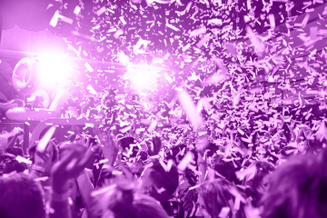 Confetti fired in the air during a in a disco. Hundreds of hands to the sky. Purple tone/background