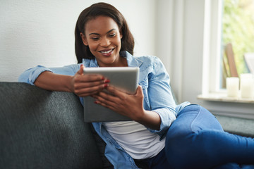Smiling African woman sitting on her sofa using a tablet