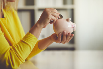 Woman inserts a coin into a piggy bank - 181148786