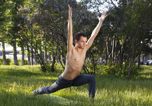  young strong man is engaged in yoga and gymnastics in the park, morning exercises,