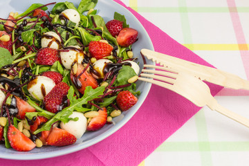 summer salad bowl with strawberries, field salad, beetroot, arugula, mozzarella and pine nuts with balsamic vinegar and cutlery