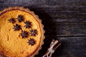 Traditional American pumpkin pie with spices on an old wooden background.