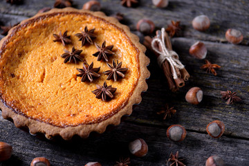 Traditional American pumpkin pie with spices on an old wooden background.