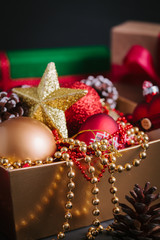Composition with gift and Christmas decorations in golden box on black background