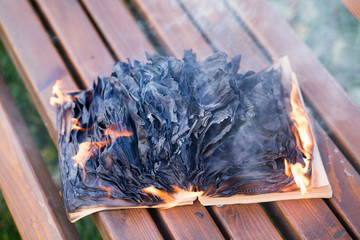 The burning book lies on a wooden bench. The book burns.