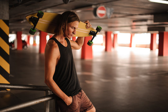 Attractive long-haired guy looking down and holding a longboard