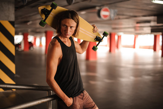 Attractive long-haired guy looking away and holding a longboard