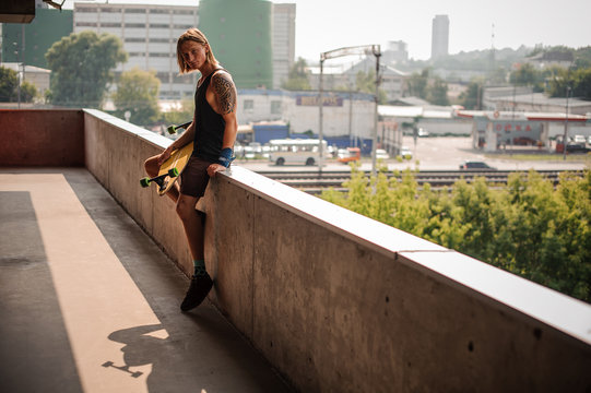 Handsome long-haired guy sitting on the parapet with longboard