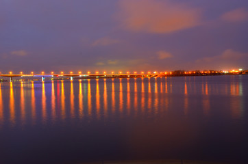 Obraz premium Night city embankment in Perm and bridge through the Kama river, lit by lanterns, the reflection of light in water.