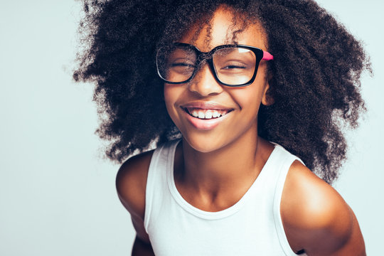 Laughing African girl in glasses standing against a gray backgro