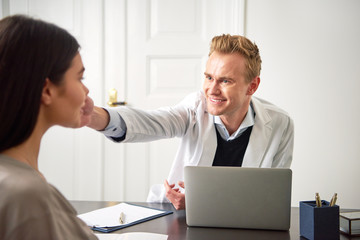 Male cosmetologist touching woman face at laptop during consultation