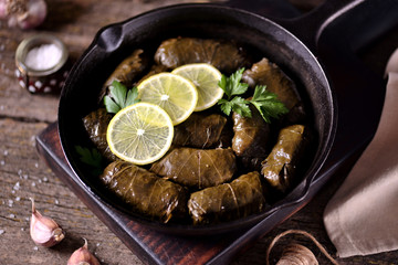 Dolma, stuffed grape leaves with rice and beef minced meat in a cast-iron frying pan on an old wooden background. Middle Eastern cuisine.