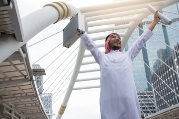 Arabian businessman holding the briefcase and raising arms standing in downtown with job to success...
