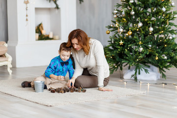 A mother and a son hugging and having fun in front of the fir-tree with candles. New year's eve. Christmas eve. Cozy holiday at the fir-tree with lights and gold decor.