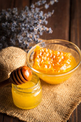 Honey dripping from a wooden honey dipper in a jar on wooden grey rustic background