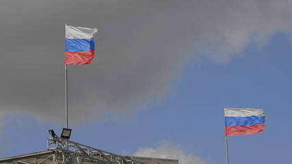 Russian flag on the flagpole waving in the wind against a blue sky with clouds