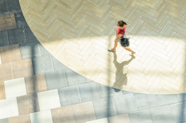 Silhouette of a walking woman with long shadow from above. Abstract background of blur in motion figure of a young woman in a public building hall top view. Blurred Abstract Background.