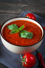 Chili tomato soup with sour cream sauce, cottage cheese, basil and red hot peppers on wooden background. Healthy, vegan and dieting lunch and dinner concept.