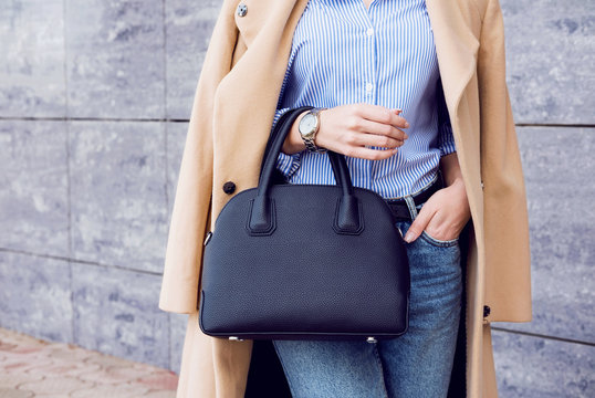 Trendy woman in beige coat and jeans with black big bag