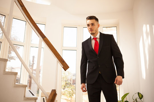 Young Business Man In Suit And Red Tie In Office Building Interior Walking Down The Stairs