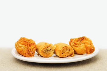 Traditional Oriental sweets closeup with chopped nuts and honey syrup on white plate. Selective focus.  Copy space at the top of the frame