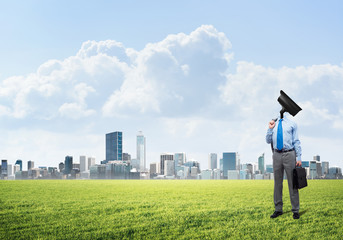 Camera headed man standing on green grass against modern cityscape