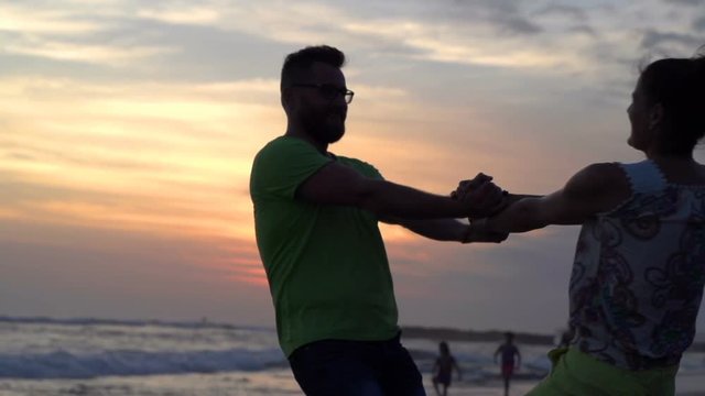Happy cuple going round on the beach during sunset, steadycam shot, slow motion shot at 240fps

