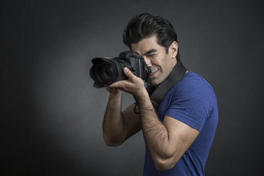 Fotografo con capelli neri e maglietta blu è intento a scattare una fotografia - sfondo scuro