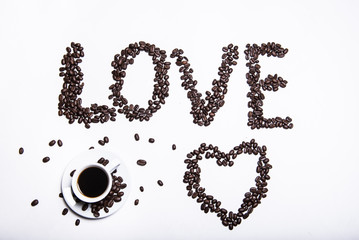 Morning coffee, the concept of still life. An inscription made of coffee beans on a white background next to a cup of coffee. Heart made of coffee beans and inscription love