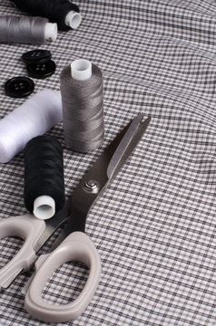 Tools and accessories for sewing. Sewing thread, scissors, buttons on gray textile background