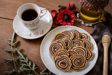 Spiral Cookies with a white cup of coffee and red flower on a wooden table. Handmade biscuits